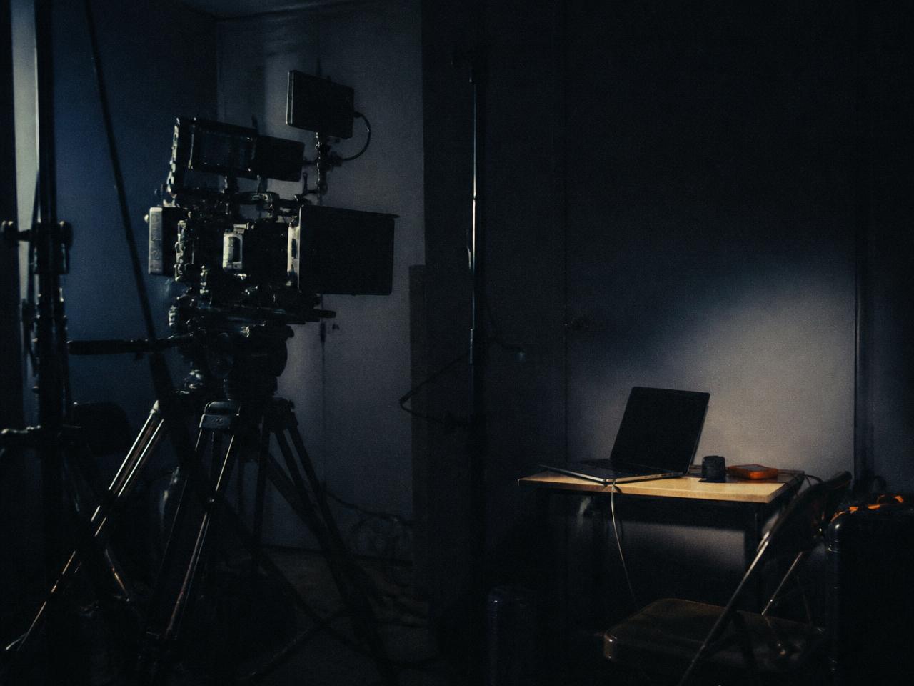 A full film production rig set up in a studio beside a single laptop on a small desk