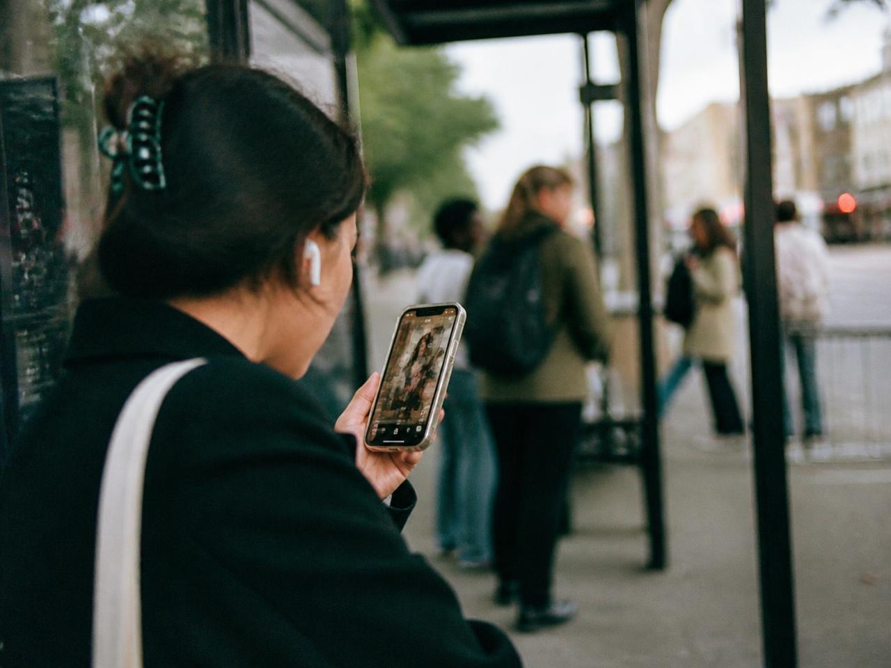 A commuter at a bus stop watching a video ad play on her phone