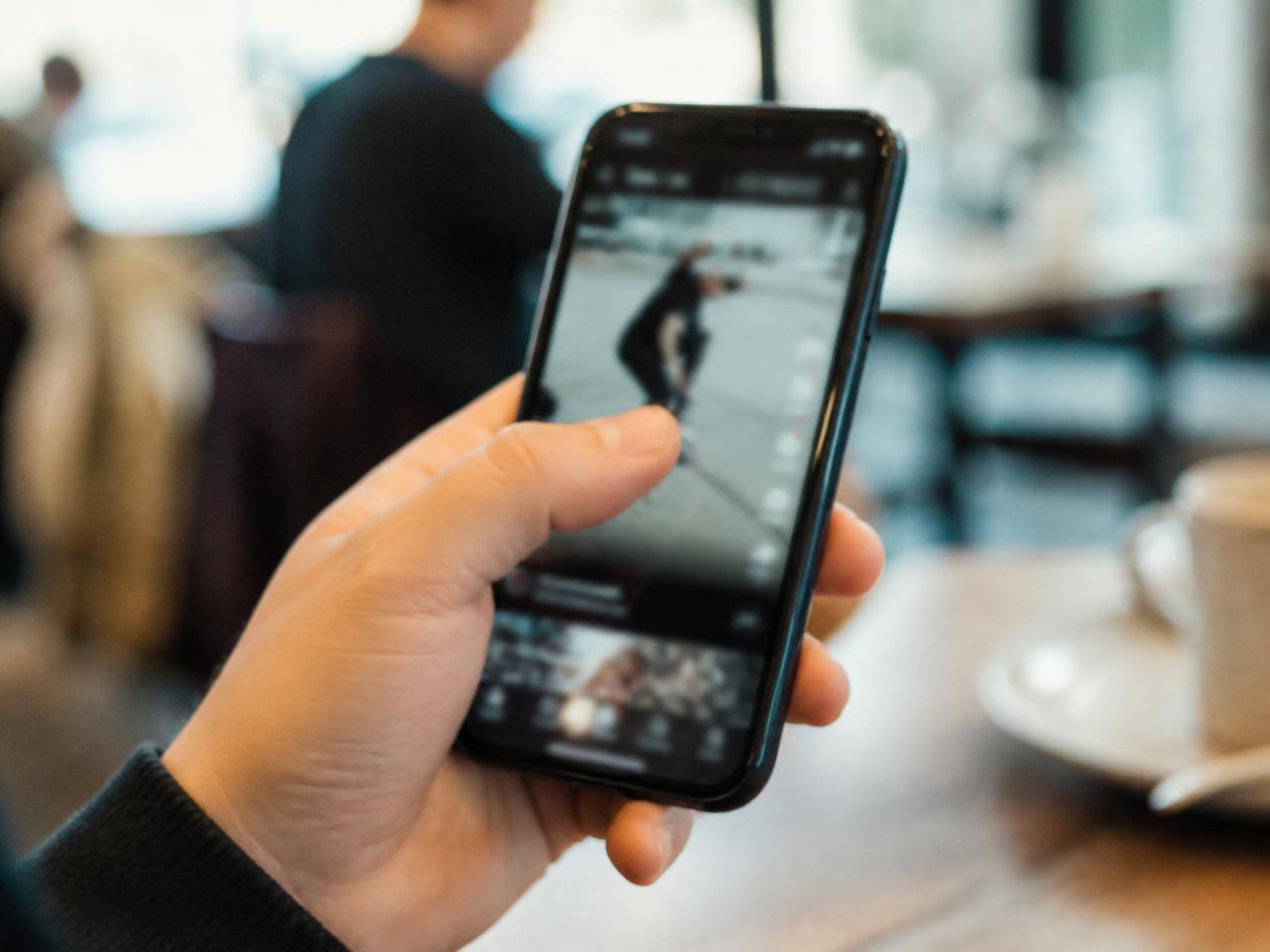 A hand holding a phone with a thumb paused mid scroll on a vertical video in a social feed